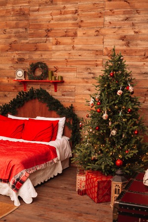 Christmas fir and the bed. New Year interior of room with bed and Christmas tree. Beautiful holdiay decorated room with Christmas tree and presents under it. Xmas background.の写真素材