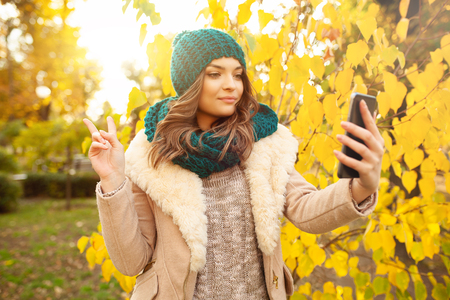 Young girl takes a selfie on the backgroung autumn beautiful leaves. Autumn concept. Videoblogerの写真素材