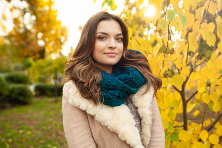 A beautiful young girl in a hat and scarf walks through the autumn park on the background of brightly colored leaves. Autumn concept, fashion and style.の写真素材