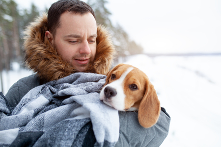 A young man wrapped his best friend Beagle dog in a warm blanket to warm him in a cold snowy winter. Animal protectionの写真素材