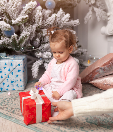 Mom gives a gift to her beloved little daughter for the new year. Christmas tree on the background Merry Christmass and Happy New yearの写真素材