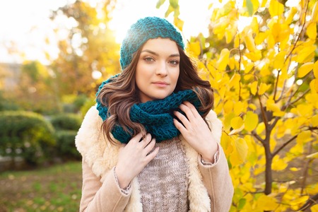 A beautiful young girl in a hat and scarf walks through the autumn park on the background of brightly colored leaves. Autumn concept, fashion and style.の写真素材