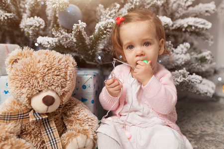 A little girl is playing with a garland with a New Year tree. Danger. Disobedient child. Good New Year spirit.の写真素材