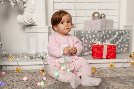 Merry Christmas and Happy New Year Beautiful cute little girl sitting on the floor near the New Year tree. Holiday mood, childlike spontaneity and sweet atmosphereの写真素材