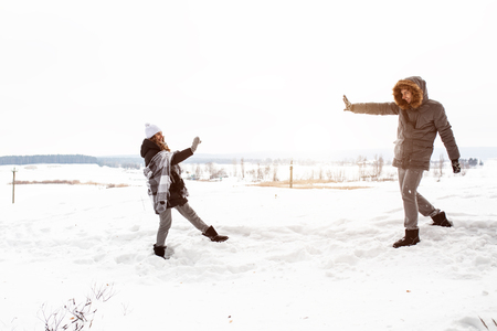 Carefree happy young couple having fun together in snow in winter woodland throwing snowballs at each other during a mock fight.の写真素材
