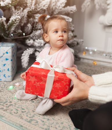 A beautiful cute little girl opens a New Year's gift. With Christmas tree on the background Merry Christmas and Happy New Yearの写真素材