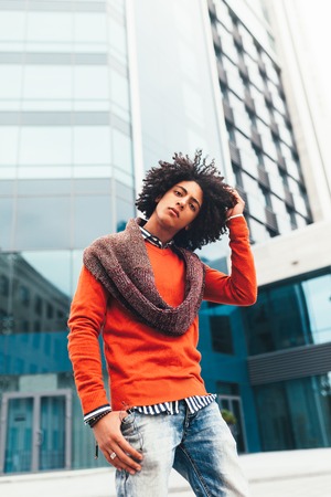 Young fashionable dressed curly black African American with glasses walks through the streets against a skyscraper. A student with a backpack standing against the background of glass wallsの写真素材