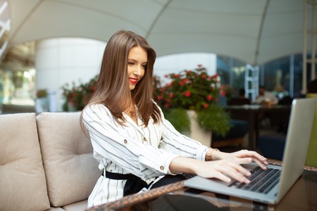 Outdoor portrait of caucasian businesswoman using wireless Internet connection on laptop and gadgets, messaging via popular social networks, dressed casually. People and technology concept.の写真素材