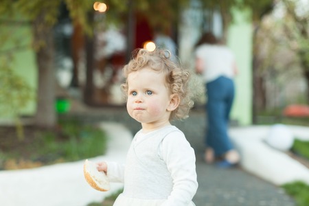 Beautiful curly little girl in the white dress holding her snack in the square