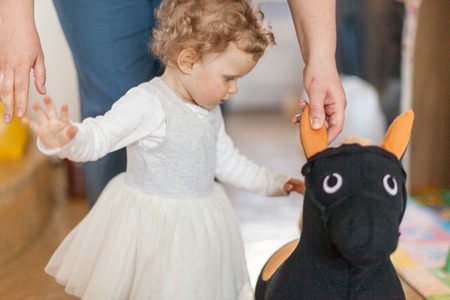 Curly little girl going to a toy and father standing behind and helping her to walk