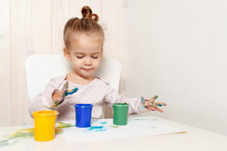 Beautiful little girl draws with finger paints on a white sheet of paper. Creative child development in kindergarten or free time at home.の写真素材