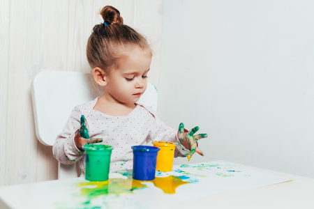 Beautiful little girl draws with finger paints on a white sheet of paper. Creative child development in kindergarten or free time at home.の写真素材