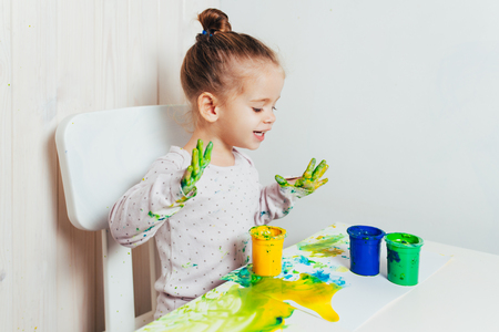 Beautiful little girl draws with finger paints on a white sheet of paper. Creative child development in kindergarten or free time at home.の写真素材