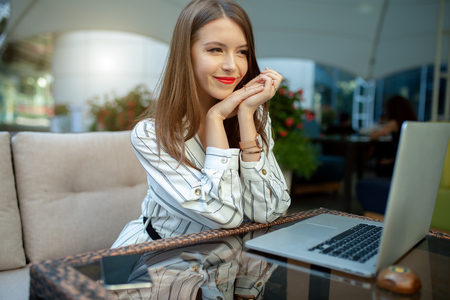 Outdoor portrait of caucasian businesswoman using wireless Internet connection on laptop and gadgets, messaging via popular social networks, dressed casually. People and technology concept.の写真素材