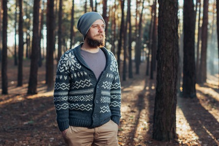 A young man with a beard walks in a pine forest. Portrait of a brutal bearded man. Autumn forest tourism conceptの写真素材