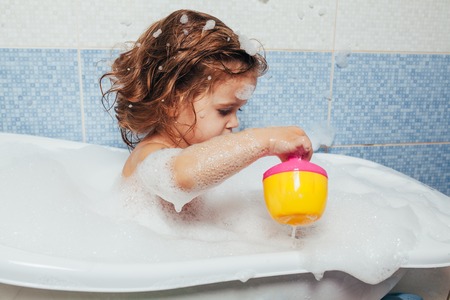 Beautiful little girl taking a bath at home. A cute baby is sitting in the bathroom and playing with toys and water. Personal hygiene for children. Daily hygiene.の写真素材