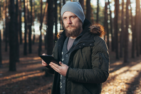 Close up portrait of adult male hiker using digital tab and looking for location during hike in nature. man on hike using digital tablet for navigation. Spring autumn seasonの写真素材
