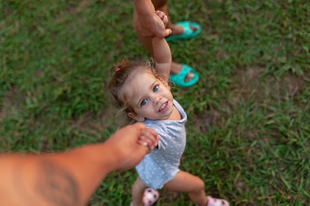 View from above of beautiful family, pretty mother, father and daughter, toddler, baby, looking up at the camera, on field, nature backgroundの写真素材