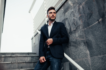 Young stylish businessman man with a beard in a fashionable suit and jeans. Modern image of business youth. It stands on the background of marble walls.の写真素材