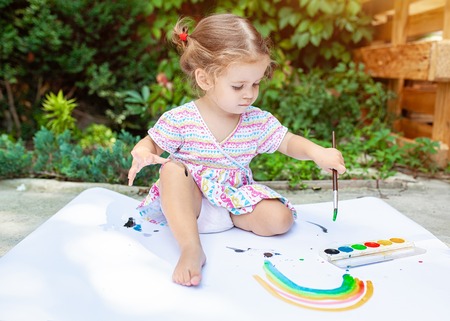 Portrait of little blonde girl painting, summer outdoor. Backyard playing kid.の写真素材