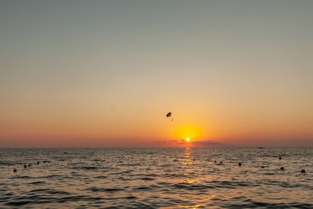 Silhouette of powered paraglider soaring flight over the sea against marvellous orange sunset sky. Paragliding - recreational and competitive adventure sportの写真素材