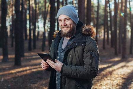 Close up portrait of adult male hiker using digital tab and looking for location during hike in nature. man on hike using digital tablet for navigation. Spring autumn seasonの写真素材
