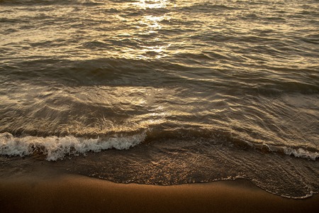 Close up beach wave at sunset. Sun reflecting on serene beach. Soft focus.の写真素材