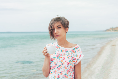 Beautiful woman with short haircut relax during exotic vacation on the beach enjoying sweet coffee or teaの写真素材