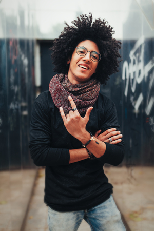 A young handsome mixed race African American man stands near a mirror wall showing a sign I love you. Afro hairstyle. Student and youth culture.の写真素材