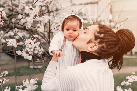 Little baby with her young mother in the blossoming Spring gardenの写真素材