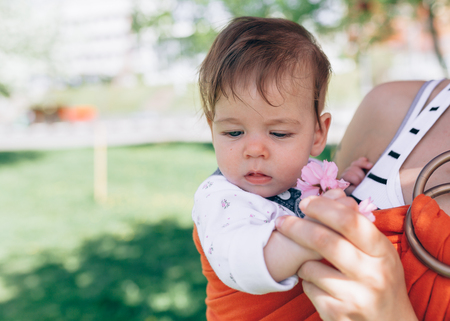 Mother carry a infant baby in wrap sling in park. Springtime. Concept of natural parenting Happy family spring conceptの写真素材