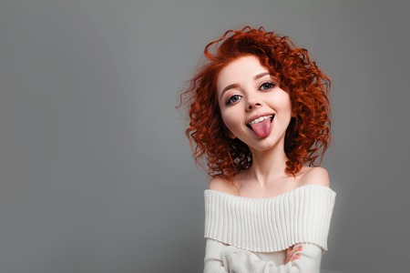 Funny redhead curly girl with big head shows tongue. Caricature stylization of female logic. Young blogger. female psychologyの写真素材