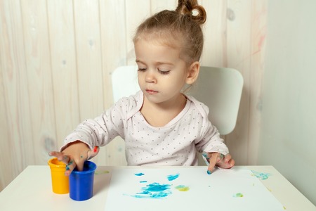 Beautiful little girl draws with finger paints on a white sheet of paper. Creative child development in kindergarten or free time at home.の写真素材