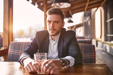 Handsome young businessman sitting in a summer outdoor cafe on the background of the evening sunset at the negotiating table.の写真素材