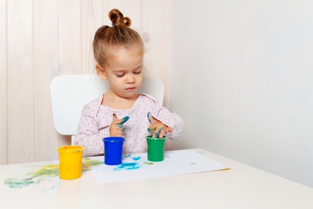 Beautiful little girl draws with finger paints on a white sheet of paper. Creative child development in kindergarten or free time at home.の写真素材