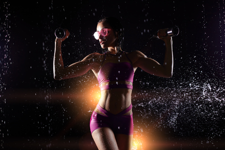 athletic woman pumping up muscles with dumbbells Beautiful athletic caucasian woman lifts dumbbells in aquastudia against a background of splashing water. Freshness sport motivationの写真素材