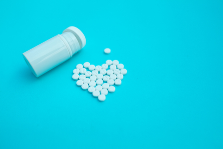 medicine, healthcare and pharmacy concept - pills and of drugs in shape of the heart white tablets are laid out in the shape of a heart and white plastic jar on a blue background with copy spaceの写真素材