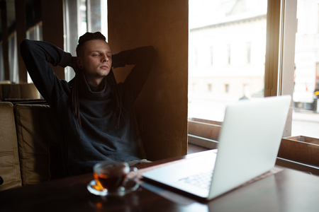 Young Businessman with dreadlock having doing his work in cafe near the big window with laptop. Youth culture. Neformal guy. Remote works. IT specialistの写真素材