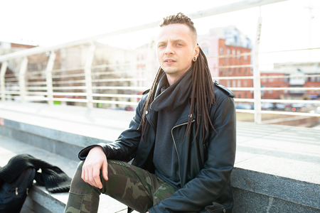rocker rock star young caucasian man with dreadlocks walking on the city street autumn day. Dressed in the leather jackedの写真素材