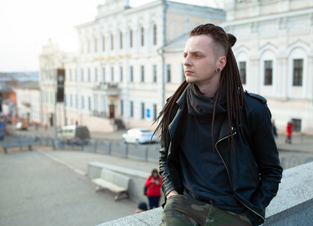 rocker rock star young caucasian man with dreadlocks walking on the city street autumn day. Dressed in the leather jackedの写真素材