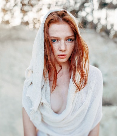 Close up portrait of a beautiful red haired girl in green medieval dress on glowing sun. Fairy tale story about brave heart woman. Amazing model looking at camera. Warm art workの写真素材