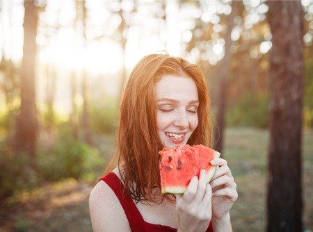 Happy young redhair woman eating watermelon on the nature. Youth lifestyle. Happiness, joy, holiday, beach, summer concept.の写真素材