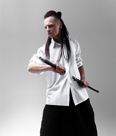 Young man dressed in the white shirt with dreadlocks holding a samurai sword. Glamour photo. Studio shooting. business man with Japanes swordの写真素材