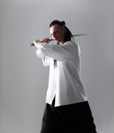 Young man dressed in the white shirt with dreadlocks holding a samurai sword. Glamour photo. Studio shooting. business man with Japanes swordの写真素材
