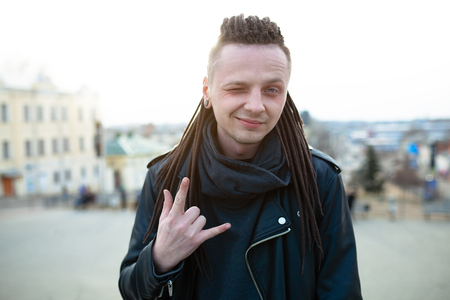 rocker rock star young caucasian man with dreadlocks walking on the city street autumn day. Dressed in the leather jackedの写真素材