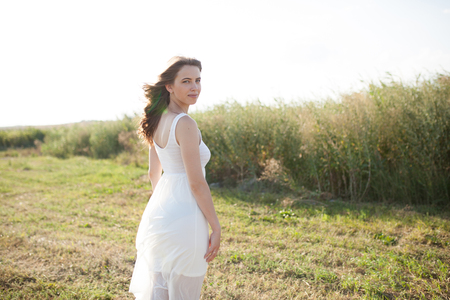 Portrait of woman on the summer field on light background. Pretty young girl. Sunny summer day. Green grass field. Summer background. Outdoor portrait, day light. Rural landscape.の写真素材