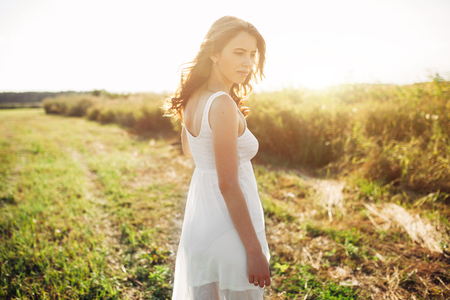Portrait of woman on the summer field on light background. Pretty young girl. Sunny summer day. Green grass field. Summer background. Outdoor portrait, day light. Rural landscape.の写真素材