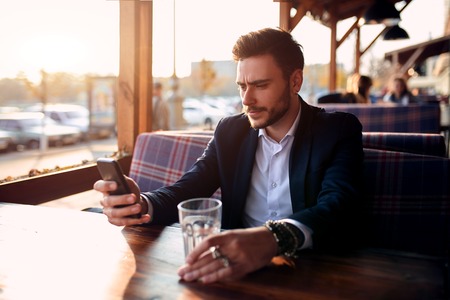 Handsome young businessman sitting in a summer outdoor cafe on the background of the evening sunset at the negotiating table.の写真素材