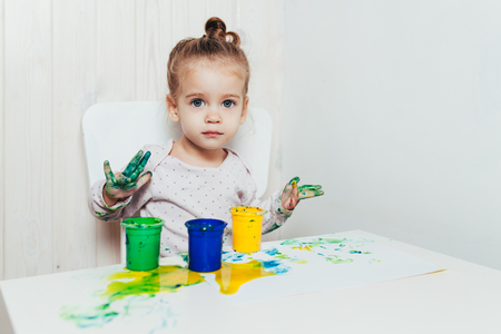 Beautiful little girl draws with finger paints on a white sheet of paper. Creative child development in kindergarten or free time at home.の写真素材