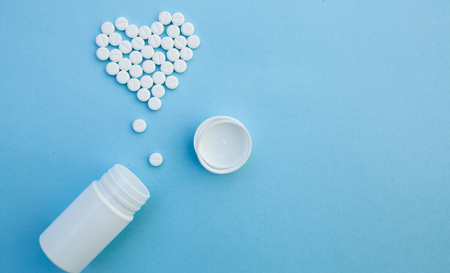 medicine, healthcare and pharmacy concept - pills and of drugs in shape of the heart white tablets are laid out in the shape of a heart and white plastic jar on a blue background with copy spaceの写真素材